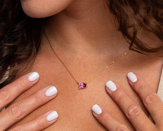 Gold necklace with a pink gemstone worn by a person with white nail polish.