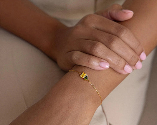 Gold bracelet with a green gemstone on a wrist against a beige background